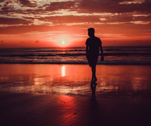 Silhouette of a person stretching against a vibrant sunrise.